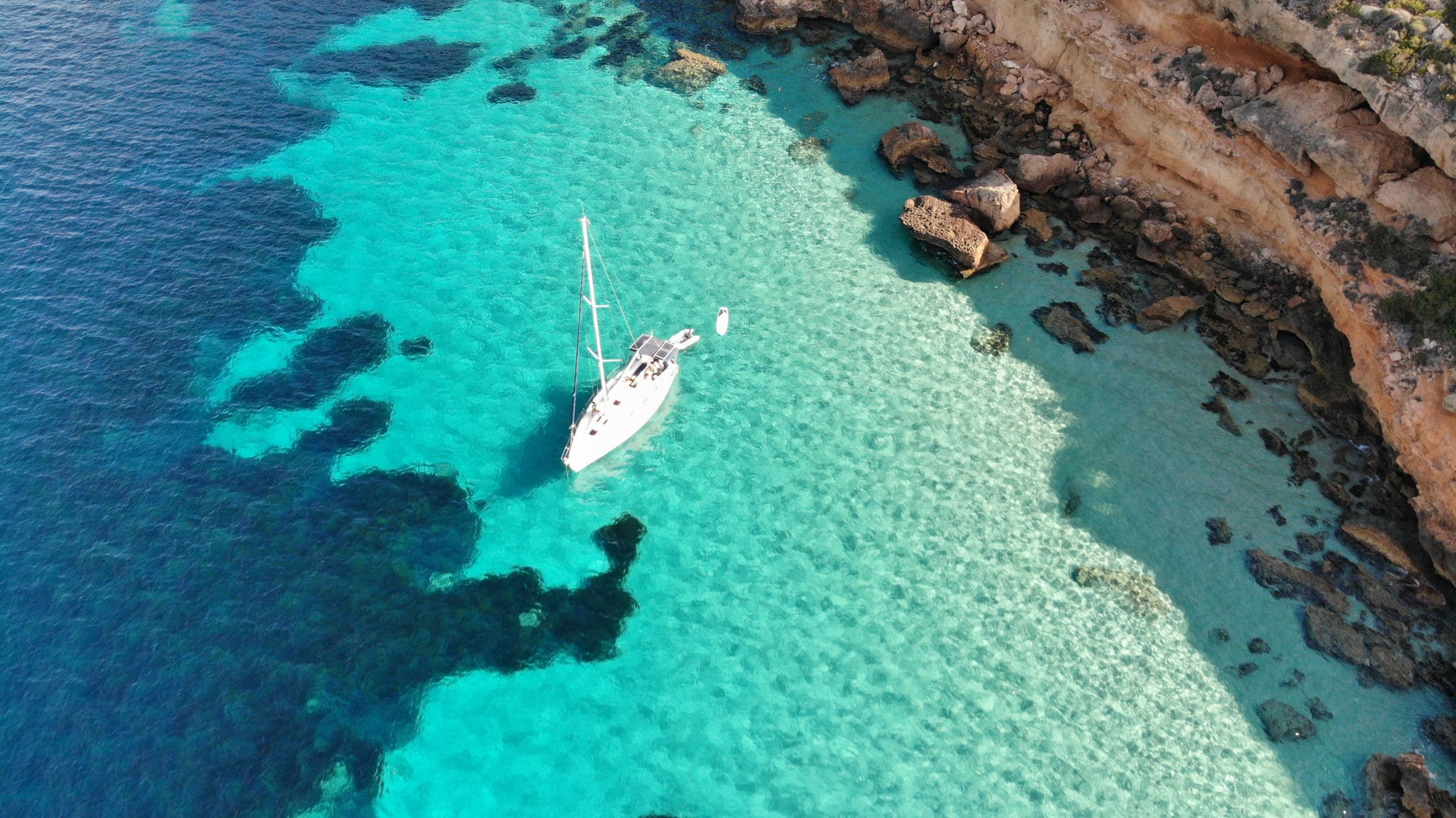 Velero fondeado en una cala de aguas turquesa en Mallorca, visto desde el aire